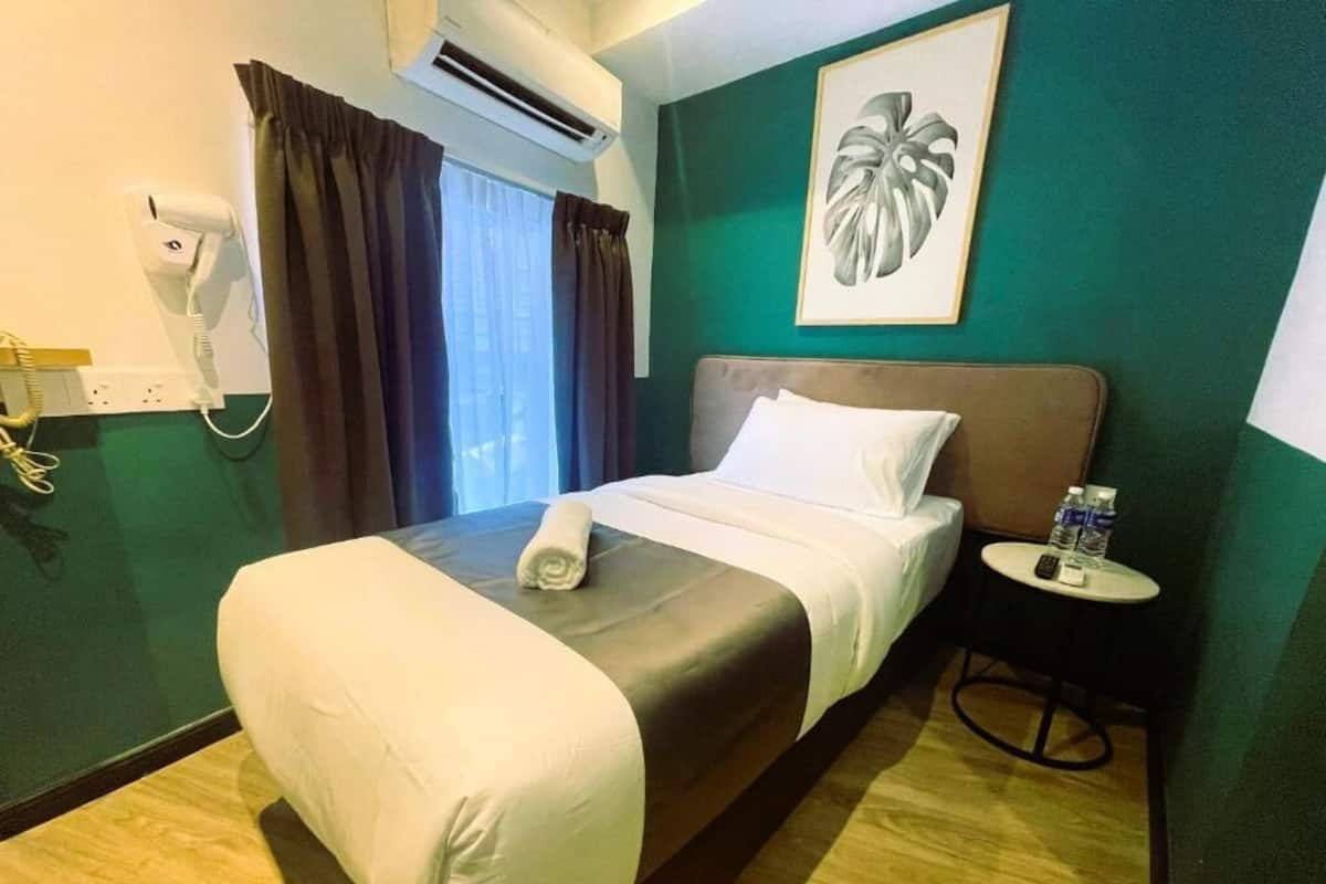 Ein Hotelzimmer mit einem Bett, einem Nachttisch mit einer Flasche, einem Föhn und einem Bild an der Wand.