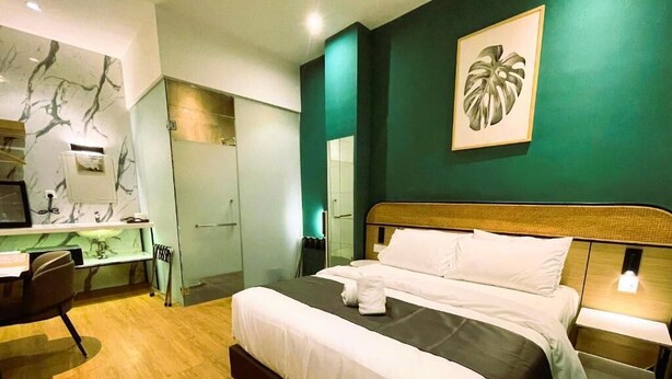 A hotel room with a bed, bedside table, desk, chair, and a large mirror. - Enclave Hotel Kuala Lumpur (Kuala Lumpur)