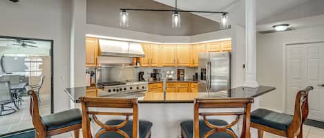 A modern kitchen with wooden cabinets, a central island, and a dining area with wooden chairs.