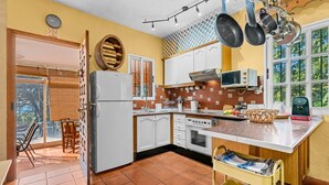 A kitchen with white cabinets, a refrigerator, a stove, and a microwave. There is a window with a view of trees and a door leading outside. - Estepona Mirador Country House (9 km from the beach) (Málaga)