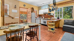 A kitchen with a dining table, chairs, a refrigerator, stove, and hanging pots. - Estepona Mirador Country House (9 km from the beach) (Málaga)