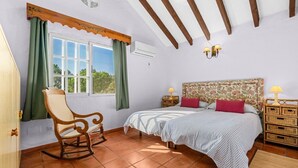A bedroom with a bed, a rocking chair, a window with curtains, a headboard, bedside tables, and a wall-mounted air conditioner. - Estepona Mirador Country House (9 km from the beach) (Málaga)