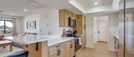 A modern kitchen with a central island, wooden cabinets, stainless steel appliances, and a large window.