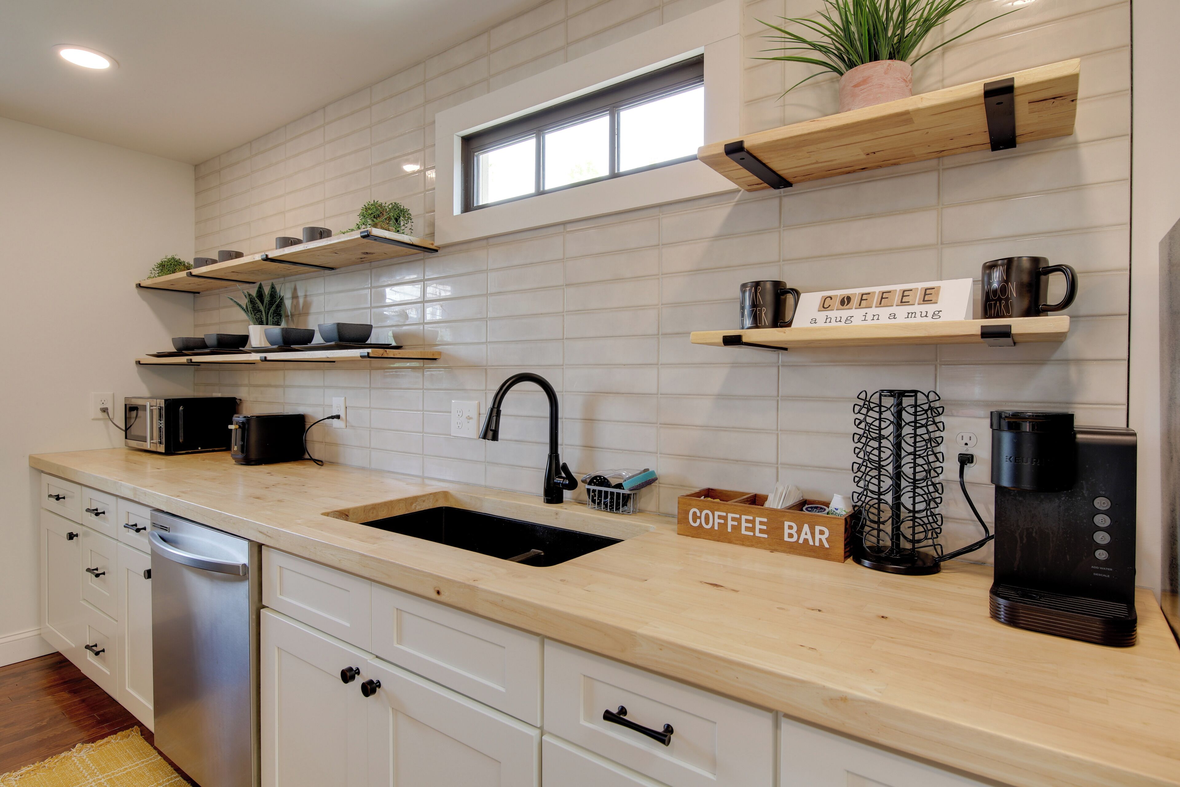 Una cocina moderna con armarios blancos, lavavajillas integrado y una zona de preparación para café.