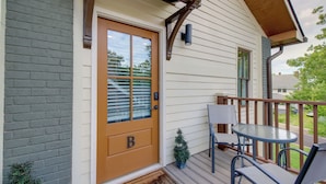 A wooden door with a 'B' marking, a small potted plant, a glass table, and a chair on a wooden deck. - Extended East Knoxville Stay, 2 Mi to Dtwn! (Knoxville)