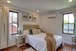Un dormitorio con cama, mesitas de noche, una ventana y un equipo de aire acondicionado.