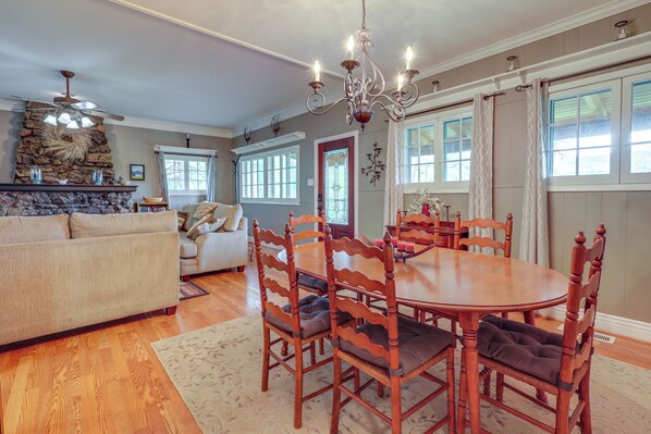 A dining area with a round wooden table and chairs, a chandelier, and a stone fireplace.