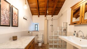 Un baño con techo de madera, ducha con paneles de vidrio, inodoro y lavamanos con gabinete de madera.