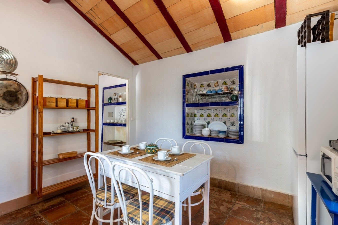 A dining area with a white table and chairs, a wooden shelf unit, and a tiled backsplash with blue accents.