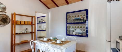 A dining area with a white table and chairs, a wooden shelf unit, and a tiled backsplash with blue accents.