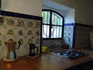 Una cocina con estufa a gas, cafetera y azulejos decorativos.