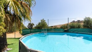 Piscina con escalera, rodeada por una valla y palmeras.