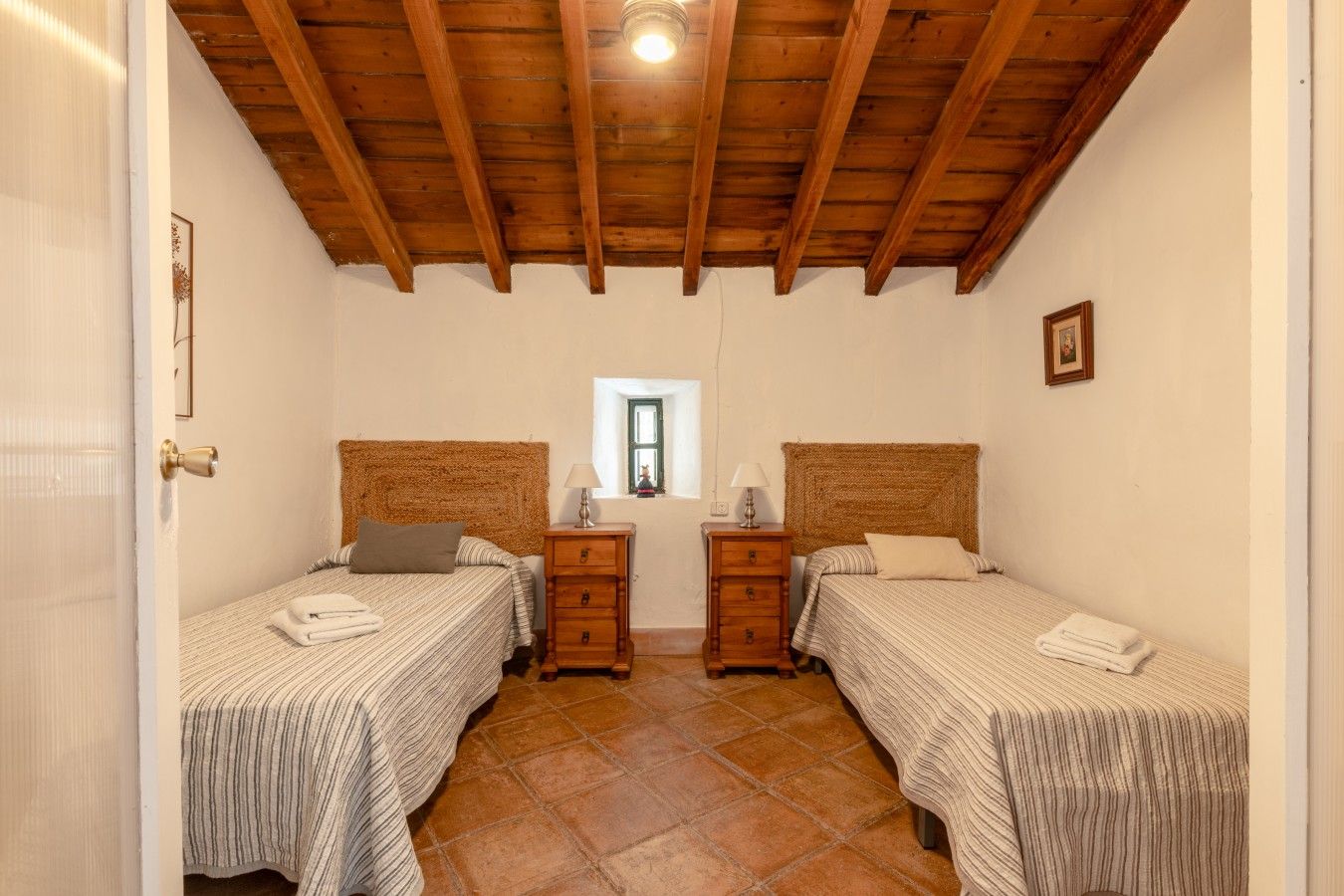 Une chambre avec deux lits, des poutres en bois au plafond, une fenêtre et une porte.