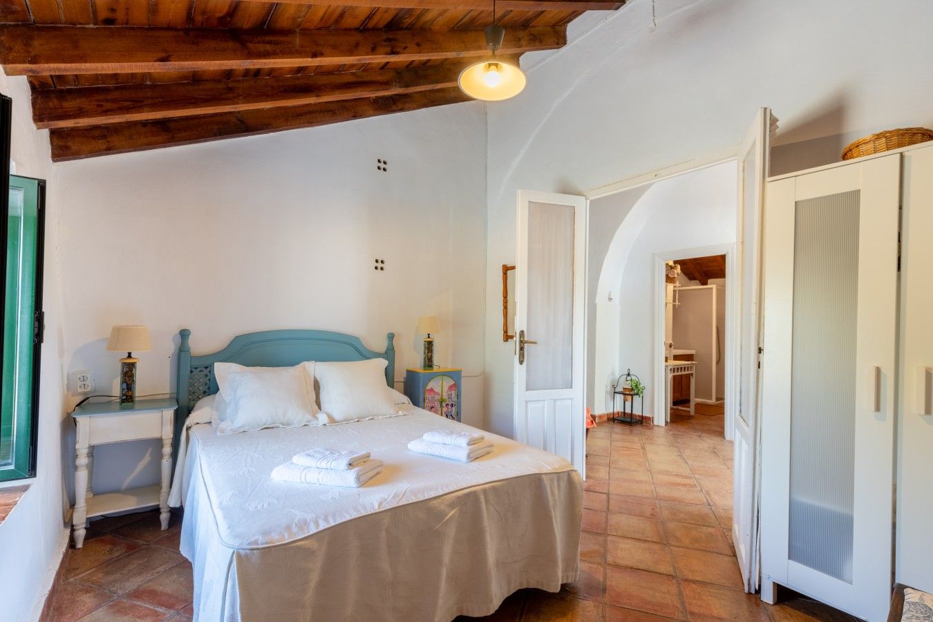 Une chambre à coucher avec un lit, des tables de chevet, une lampe et une porte donnant sur une autre pièce.