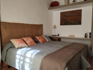 Un lit avec une tête de lit en bois, une table de chevet avec une lampe et une étagère avec des livres et des objets décoratifs.