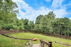 A fenced outdoor area with a wooden deck, a red object on the grass, and dense trees in the background. - Shenandoah NP Escape w/ Deck: Hike, Soak + Fish (Stanley)