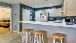 A modern kitchen with a central island, bar stools, a washing machine, and a microwave. - Unwind Poolside, Walk to Beach! Ozarks Getaway (Osage Beach)