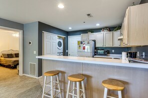 Uma cozinha moderna com ilha central, banquetas, máquina de lavar e micro-ondas.