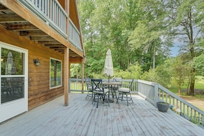Eine Holzdielen-Terrasse mit Tisch und Stühlen, umgeben von einem Geländer, mit Blick auf ein bewaldetes Gebiet.