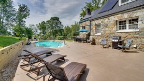 Ein Steinhaus mit Swimmingpool, Gartenmöbeln und Grillplatz.