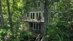 Una casa en el árbol con terraza, construida sobre un árbol, y un nivel inferior con banco.