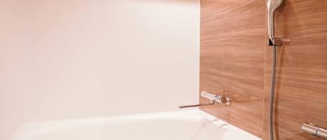 A bathroom with a white bathtub, a shower with a handheld showerhead, and wooden wall panels.