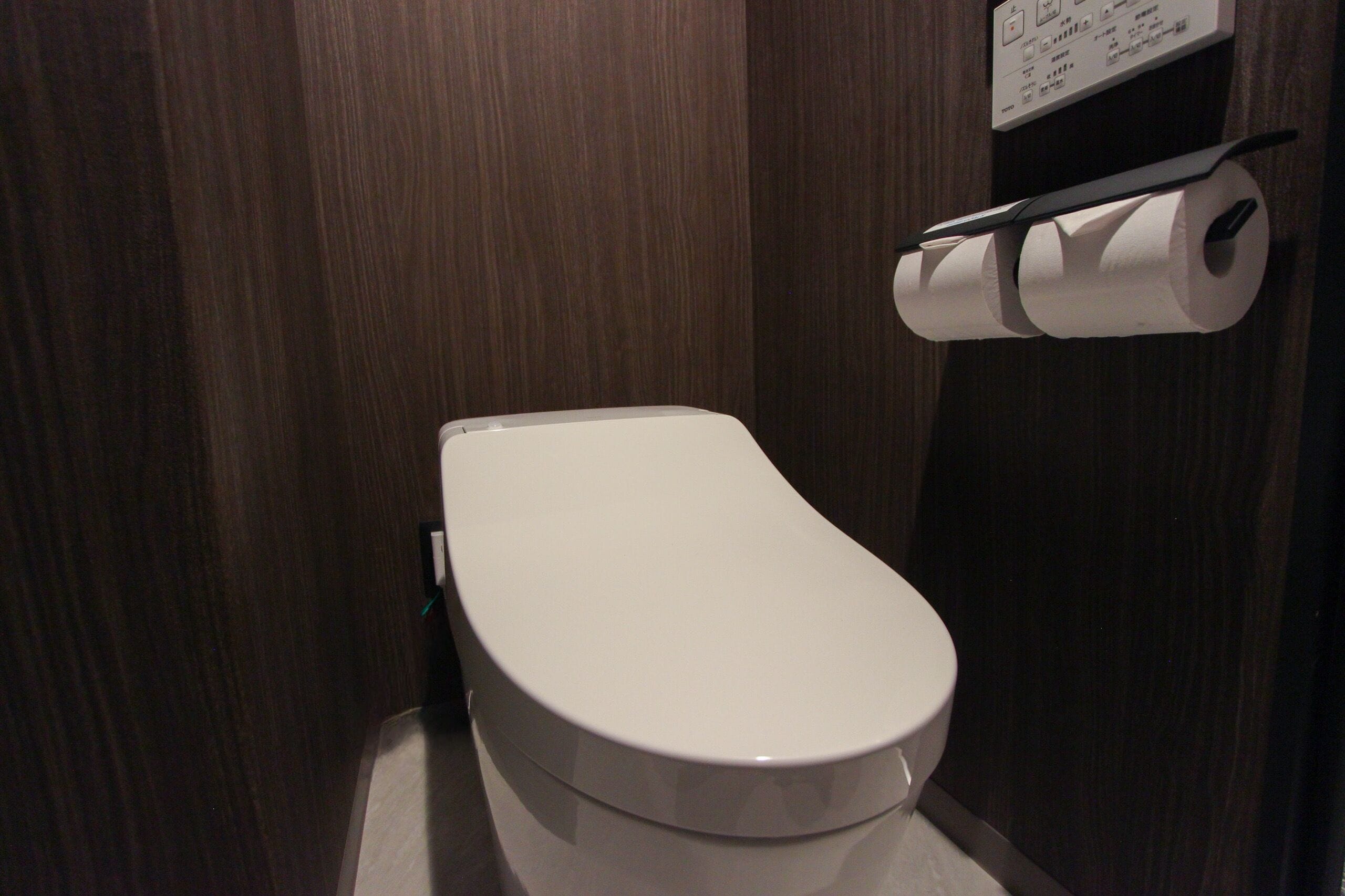 A white toilet in a wooden-finished bathroom with a toilet paper holder on the wall.