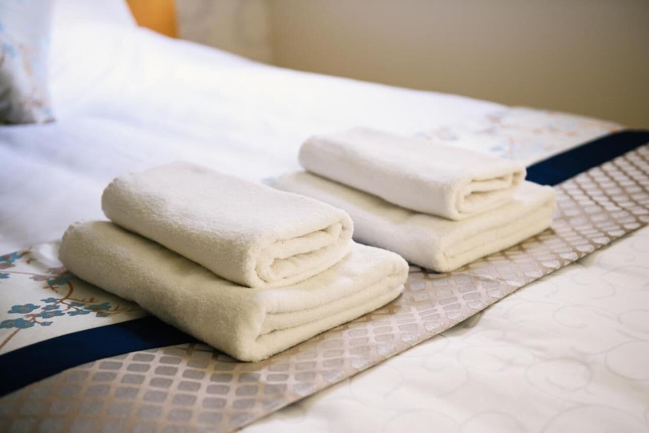 Un llit ben fet amb tovalloles blanques netejades i un llençol estampat.