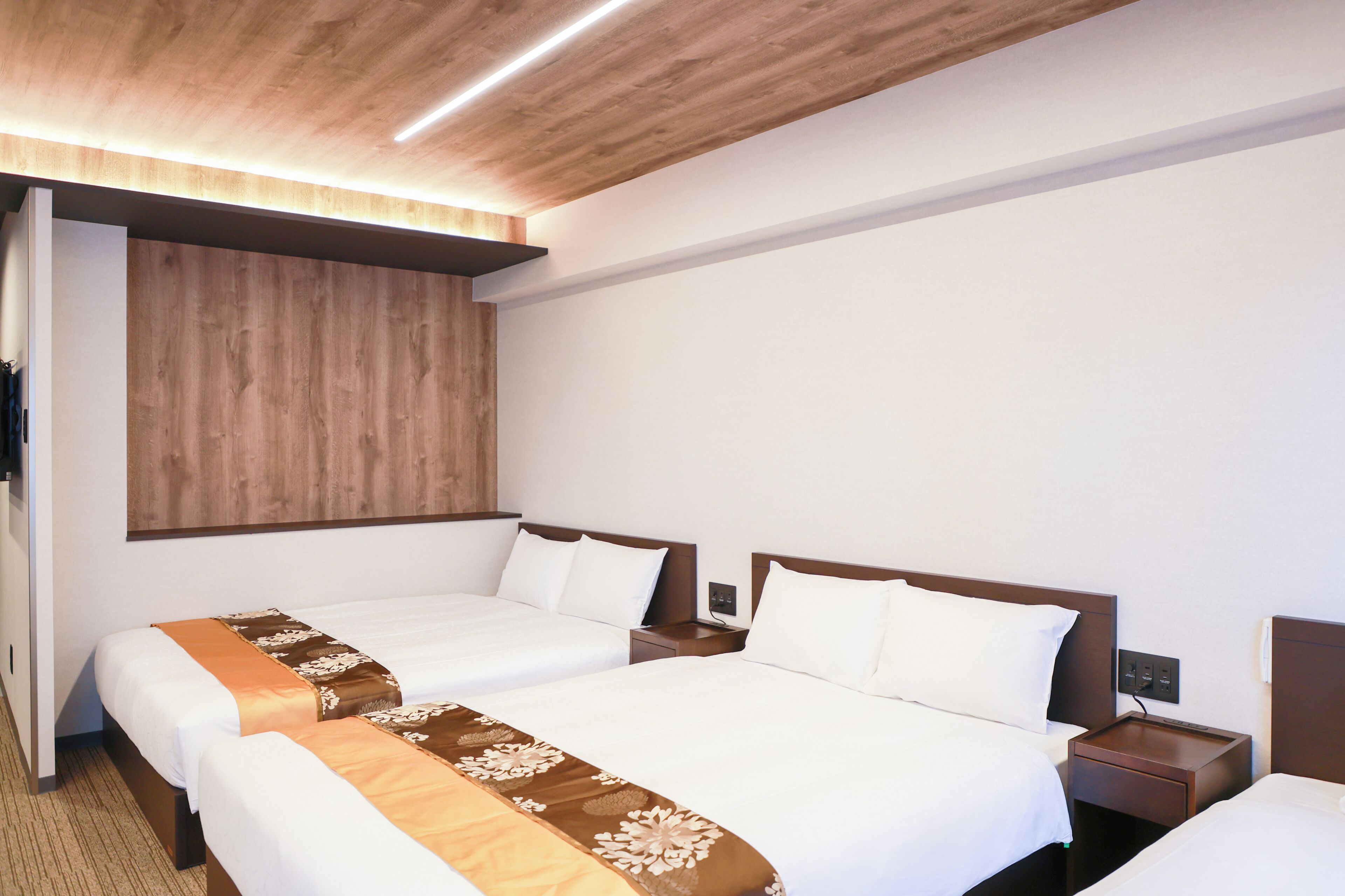 A hotel room with two beds, wooden headboard, bedside tables, and a built-in wooden panel on the wall.