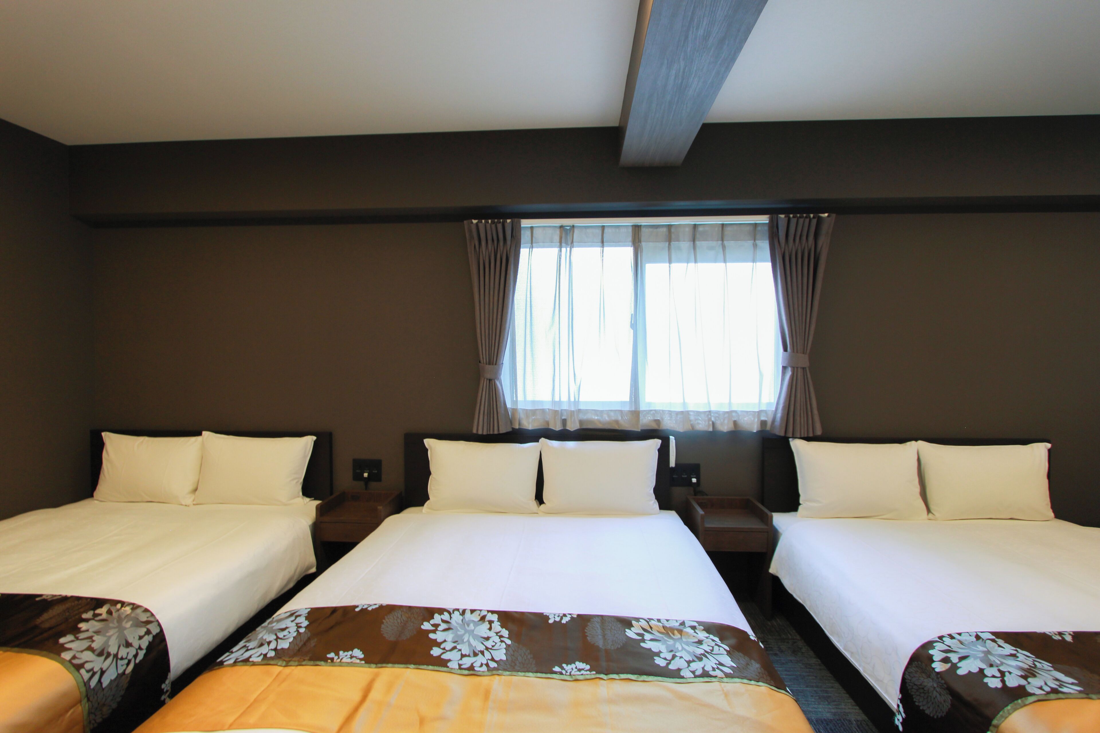 A hotel room with two beds, a window with curtains, and a bedspread with a floral pattern.