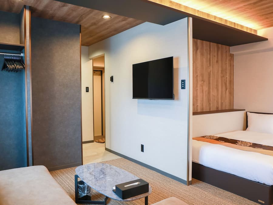 Quarto de hotel moderno com uma cama, televisão de tela plana, uma mesinha e um espaço de estar.