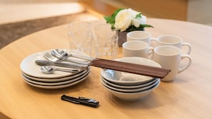 A neatly set dining table with plates, cutlery, and cups, accompanied by a small vase with a white flower. - INNEST HAKATA (Fukuoka City)