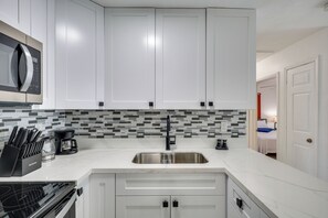 Una cocina moderna con armarios blancos, un lavamanos de acero inoxidable, un grifo negro y un microondas sobre la encimera.