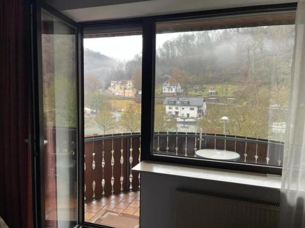 A balcony with a view of a residential area, a window with a metal railing, and a radiator.