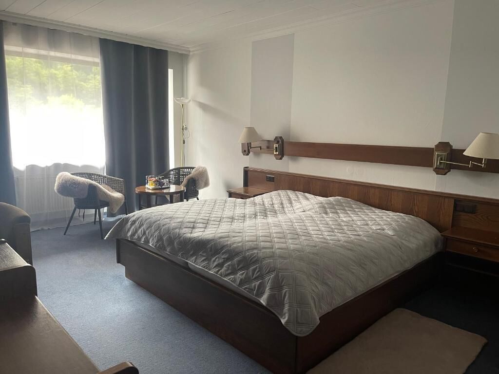 Habitació d'hotel amb un llit gran, una cadira, una taula petita i una làmpada.