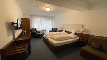 Habitación de hotel con cama, escritorio, silla, televisor y ventana con persianas.