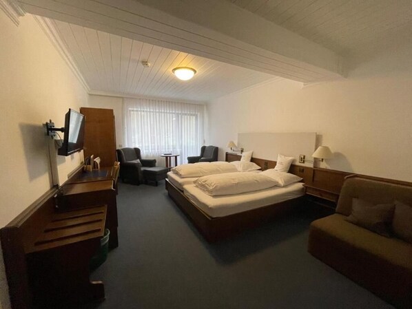A hotel room with a bed, a desk, a chair, a TV, and a window with blinds. - Hotel Balduin (Balduinstein)
