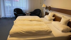 A hotel room with a large bed, two chairs, a lamp, and a view through sheer curtains.
