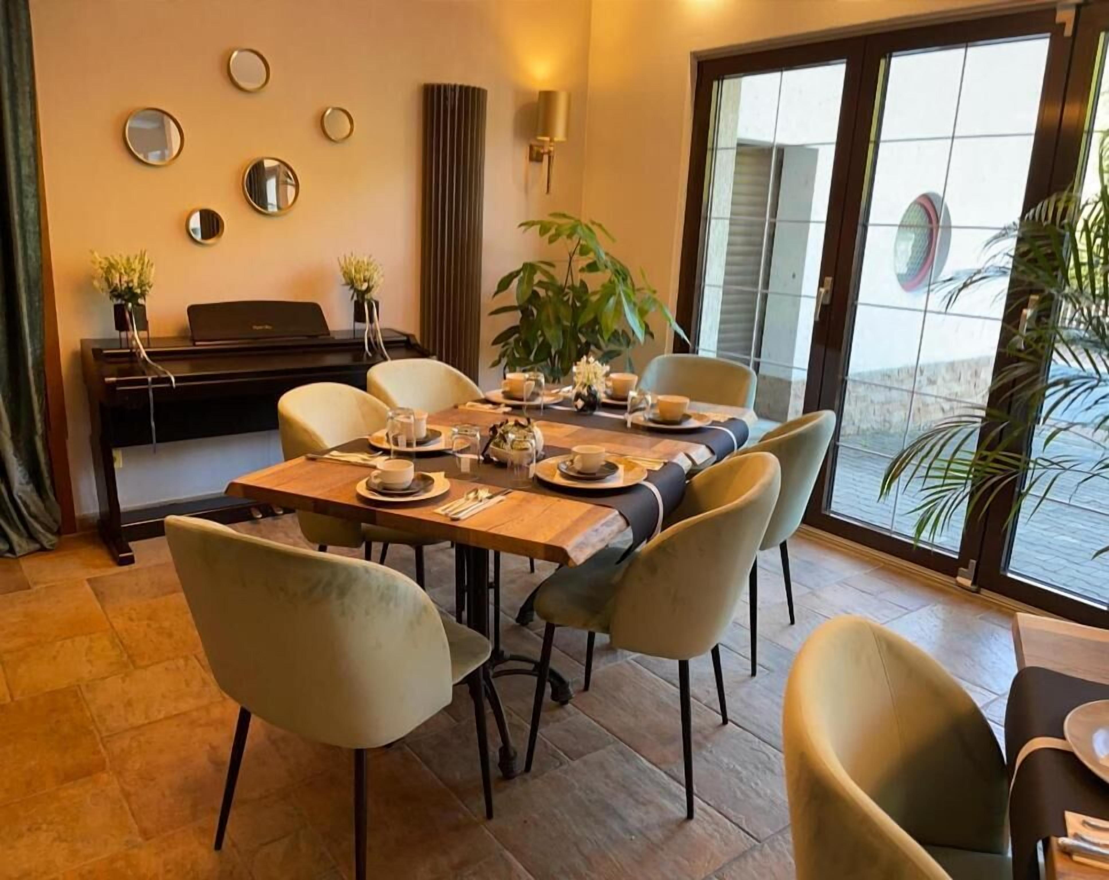 A dining area with a table set for four, chairs, a piano, and a large window with a view.