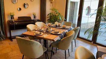 A dining area with a table set for four, chairs, a piano, and a large window with a view.