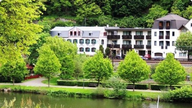 A hotel with multiple floors, a pond in the foreground, and lush greenery surrounding the property.