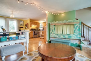 A spacious living area with a wooden dining table, a bench, a kitchen in the background, and a staircase with a stone accent wall. - Family Mashpee Eco-Retreat - Naturally Cape Cod! (Mashpee)