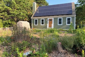 A house with solar panels, a wooden door, and a garden with various plants. - Family Mashpee Eco-Retreat - Naturally Cape Cod! (Mashpee)