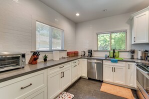 A modern kitchen with white cabinets, a stainless steel dishwasher, a built-in oven, and a window with blinds.