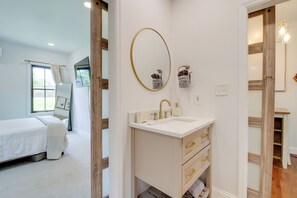 Ein Schlafzimmer mit Bett, Fenster, Badezimmer, Waschbecken, Spiegel und Handtuchhaltern.