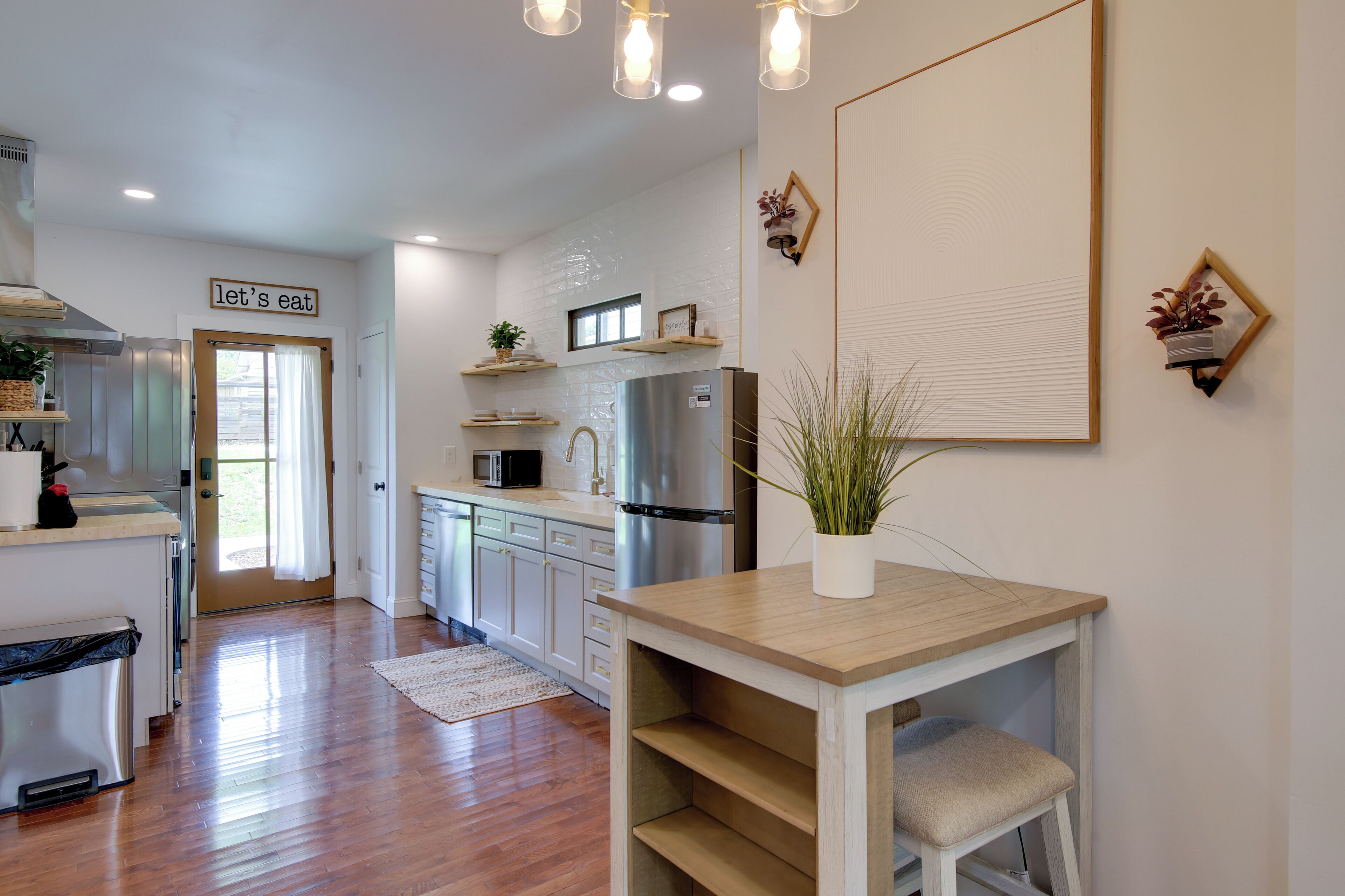 A modern kitchen with white cabinets, stainless steel appliances, and a wooden dining table.