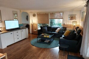 A living room with a sofa, coffee table, TV, and a dining area with a cabinet and lamp. - Holiday home with 3 bedrooms (Julianadorp aan Zee)