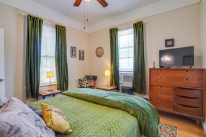 Ein Schlafzimmer mit Bett, Kommode, Fernseher und Vorhängen.