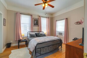Ein Schlafzimmer mit einem Bett, einem Schreibtisch, einem Deckenventilator und Fenstern mit Vorhängen.