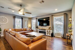 A living room with a sectional sofa, a flat-screen TV, a ceiling fan, and a fireplace. - Walk to Lake Granbury: Home w/ Fire Pit! (Granbury)
